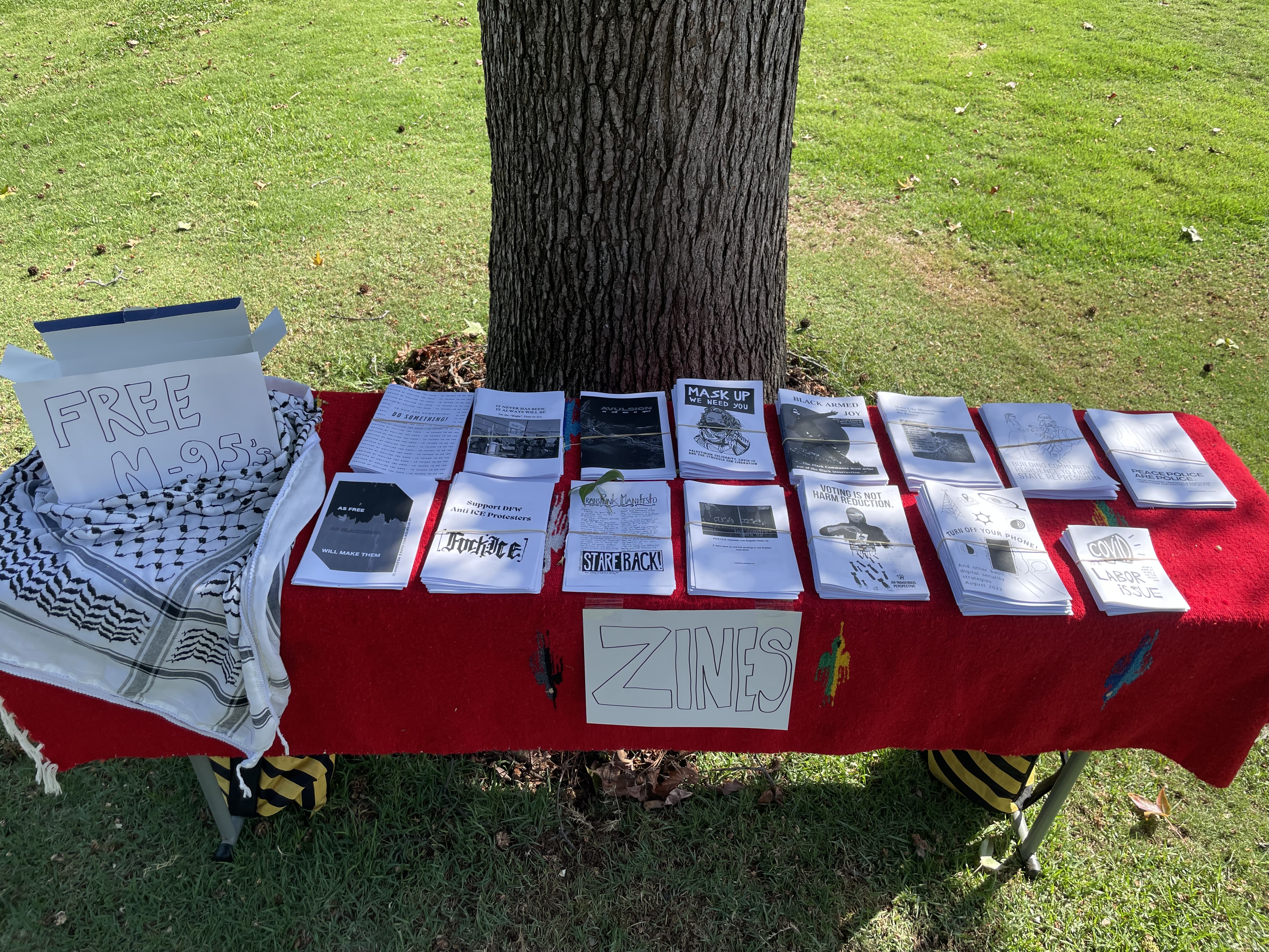 A table with several zines and N95 respirators for free distribution. There is a black and white keffiyeh next to the box marked 'Free N-95s' on the left.